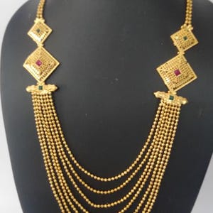 May include: A gold-toned multi-strand necklace featuring six cascading chains of small beads. The upper section includes two symmetrical diamond-shaped filigree plaques on each side, accented with small embedded red and green square-cut stones.