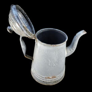 May include: A vintage white enamel teapot with a lid that is open. The teapot has a spout and a handle. The enamel has a mottled appearance.