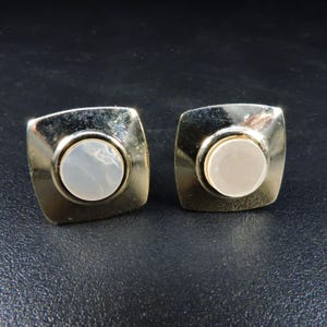 May include: A pair of gold square cufflinks with a round white mother of pearl inlay.