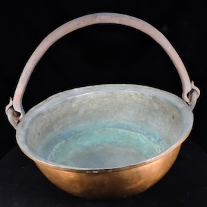 Peut inclure: Un chaudron en cuivre avec une anse incurvée en métal rouillé. L'intérieur présente des signes d'âge avec une patine aux teintes vertes et bleues. L'extérieur du chaudron est d'une couleur brun-rougeâtre chaude.