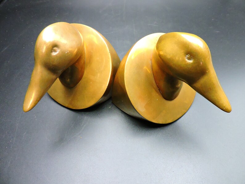May include: A pair of gold-toned metal duck bookends. The ducks are facing opposite directions and have a simple, abstract design.