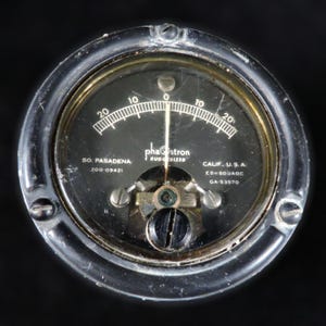 May include: A white ceramic mug with a black handle and the text "But First, Coffee" in a bold, black font. The mug is set against a blurred background, suggesting a cozy setting.