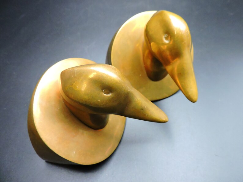 May include: Two gold-colored metal duck bookends. Each duck is perched on a round base.