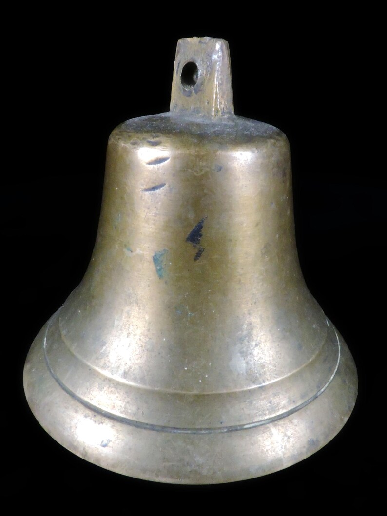 May include: A bronze bell with a flared base and a loop at the top for hanging. The bell has a slightly tarnished appearance, with some darker spots and scratches visible on the surface. The bell is a classic shape, suitable for various uses.