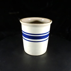 Peut inclure: Un pot en céramique cylindrique présentant une base de couleur crème avec deux bandes horizontales bleu foncé entourant la section centrale. Le récipient possède un bord lisse légèrement évasé et une construction opaque et solide.