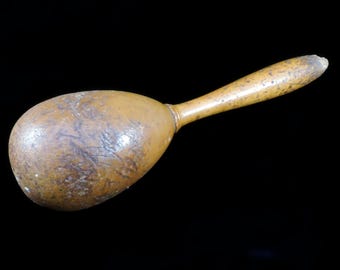 May include: A wooden egg-shaped maraca with a long, brown handle. The maraca has a rough, textured surface.