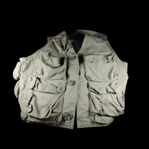 May include: An olive green vest with multiple pockets and button closures. The vest has a V-neck and a military-style design. The text "ARMY AIR FORCE" is visible on the upper right side of the vest.