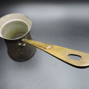 May include: A vintage brass coffee pot with a rounded body and a long handle. The handle has a hole in it and the number "10" is engraved on the handle.