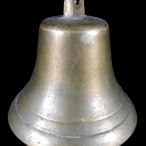 May include: A bronze-colored bell with a flared base and a loop at the top for hanging. The bell has a smooth, slightly aged appearance, suggesting it may be vintage or antique. The bell's design is simple and functional, suitable for various uses.