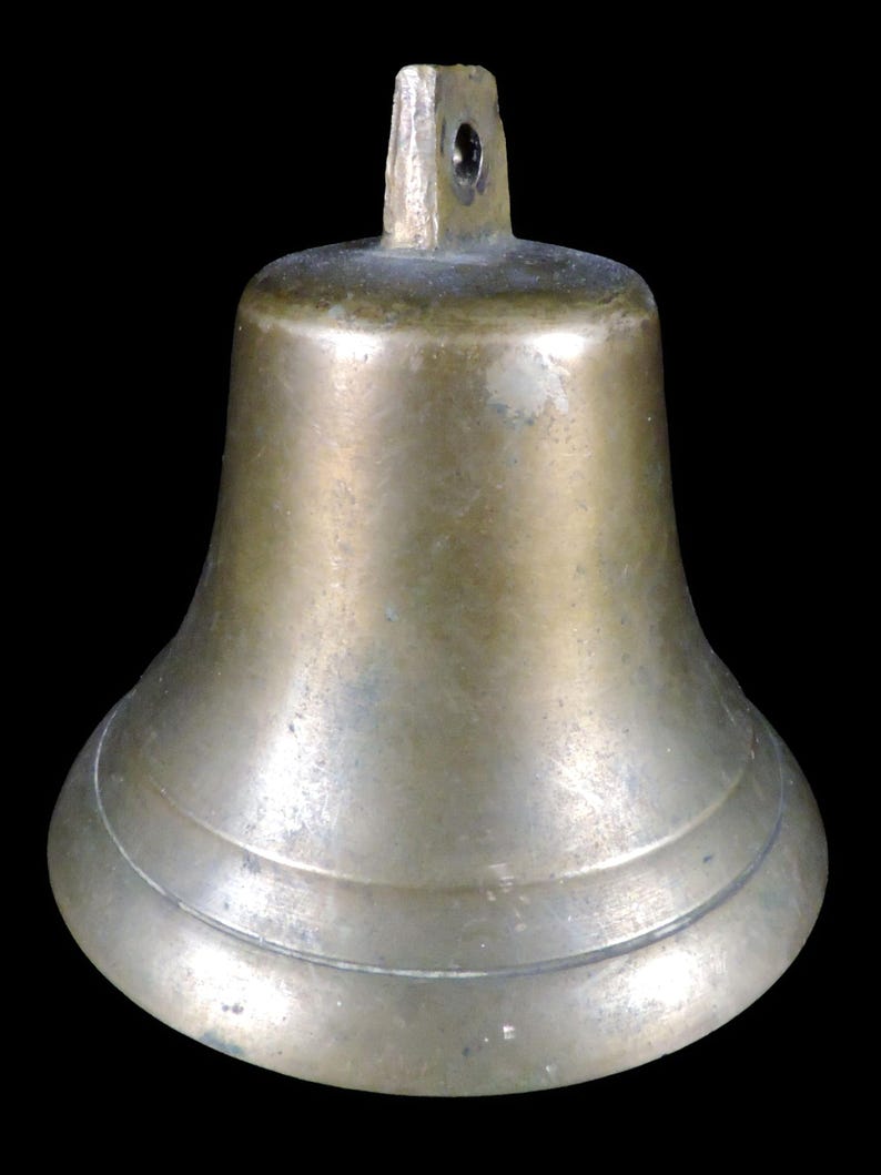 May include: A bronze-colored bell with a flared base and a loop at the top for hanging. The bell has a smooth, slightly aged appearance, suggesting it may be vintage or antique. The bell's design is simple and functional, suitable for various uses.