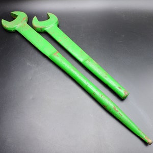 May include: Two green wrenches with a slightly distressed finish are displayed against a black background. The wrenches are long, with a tapered handle and a U-shaped head. The tools appear to be made of metal.