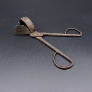 May include: Antique metal cigar cutter with a rusty finish. The cutter has two handles and a blade for cutting cigars.