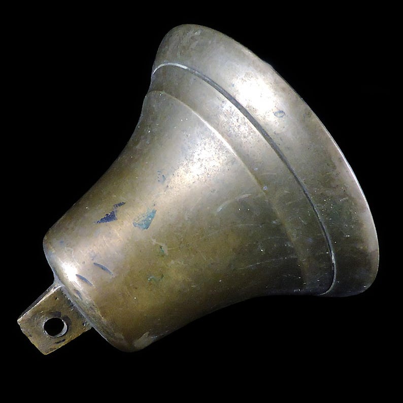 May include: A vintage brass bell with a flared shape and a small rectangular mounting bracket. The bell has a tarnished, aged appearance with visible wear and tear, and a dark background.