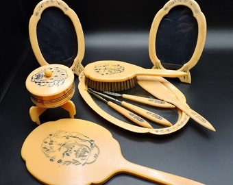 May include: A vintage ivory-colored vanity set with a brush, two mirrors, a small round container, and a large hand mirror. The set features intricate floral designs and a delicate ivory color.