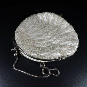 May include: A white beaded evening bag with a silver chain strap. The bag is round and has a clasp closure.