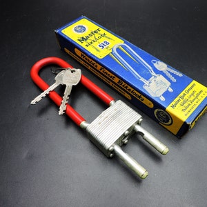May include: A red and silver Master Bike Lock 518 with two keys. The lock is in its original box, which is blue and yellow with the text "World's Finest Bikelocks" printed on it.