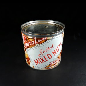 May include: A cylindrical metal can of Capitol Brand Salted Mixed Nuts. The label features a white background with red text reading Salted Mixed Nuts, a Greek key border, and an image of assorted nuts. The top of the can is a flat metal lid.
