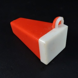 May include: A two-tone plastic object with a red body and a white end. The object has a rectangular shape with a curved handle on the white end. The object is on a black surface.