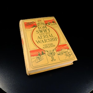May include: A yellow book with a green and red border. The title is "Tom Swift and His Aerial Warship" by Victor Appleton.