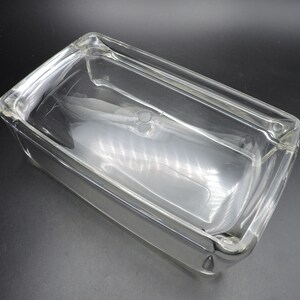 Op de afbeelding: Een rechthoekige bakvorm van helder glas met een deksel. De vorm is gemaakt van dik glas en heeft een glad, gepolijst oppervlak.