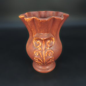 May include: A brown ceramic vase with a ruffled top and intricate gold-colored designs. The vase has a bulbous body and a flared base.