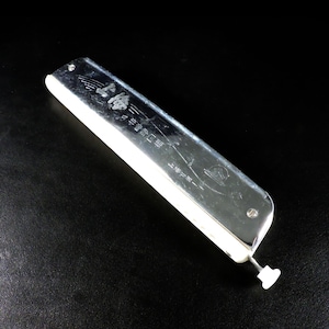 Peut inclure: Un harmonica argenté avec des détails blancs et un bouton blanc. L'harmonica porte du texte japonais gravé sur sa surface. L'instrument est rectangulaire et semble être en métal.