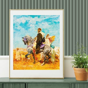 Op de afbeelding: Een ingelijst schilderij dat een groep mensen te paard in een woestijnlandschap toont. Het schilderij toont een man die een wit paard berijdt, met andere figuren die achter hem te voet lopen. De lucht is blauw met witte wolken, en de grond is zandkleurig.