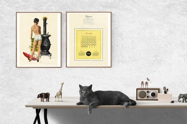 Puede incluir: Dos impresiones enmarcadas en una pared blanca, una con una ilustraci&oacute;n vintage de una mujer en traje de ba&ntilde;o blanco de pie junto a una estufa de le&ntilde;a negra, y la otra con un calendario amarillo para noviembre de 1962. Un gato gris est&aacute; acostado en una mesa de madera con una figurita de jirafa, una figurita de hipop&oacute;tamo y una radio vintage.