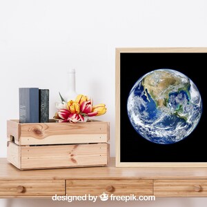 May include: A framed print of a photograph of Earth with a black background. The image shows the North American continent and surrounding oceans. The print is on a wooden table with a wooden crate, a vase, and a bouquet of yellow and red tulips.