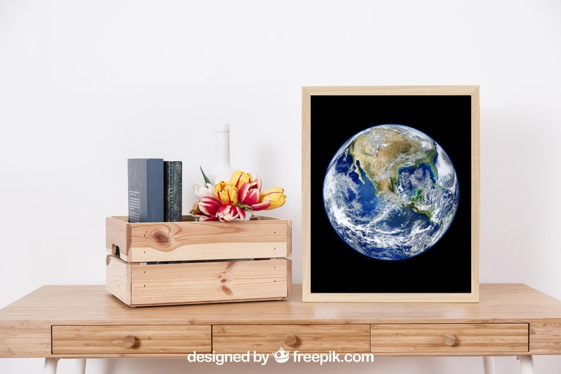 May include: A framed print of a photograph of Earth with a black background. The image shows the North American continent and surrounding oceans. The print is on a wooden table with a wooden crate, a vase, and a bouquet of yellow and red tulips.