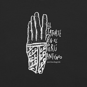 May include: A black t-shirt featuring a white graphic of a hand with a patterned wrist area. The text reads EL TATUAJE EN EL PERÚ ANTIGUO and @archaeologyink. The design uses a stippled, textured aesthetic with bold lines and high contrast.