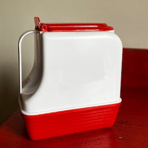 May include: A white and red plastic pitcher with a hinged lid and a handle. The pitcher has a textured bottom.