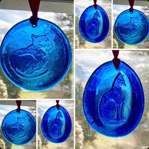 May include: Five blue glass ornaments with a cat design. Each ornament has a red ribbon for hanging.