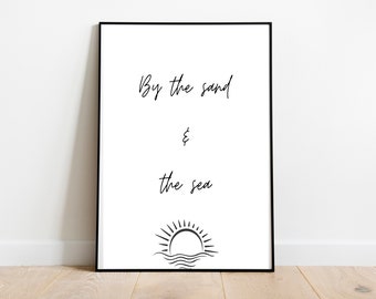 May include: A black and white printable wall art print with the text "By the sand & the sea" and a simple line drawing of a sun setting over the ocean.