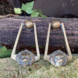 May include: Two antique brass door handles with lion head designs. The handles are triangular in shape with a rounded top and a lion head at the bottom.