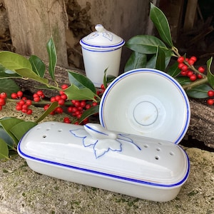 Peut inclure: Trois récipients en céramique blanche avec des bordures bleues et des motifs de feuilles. Les récipients sont un petit pot avec un couvercle, un grand bol et un plat rectangulaire avec des trous.