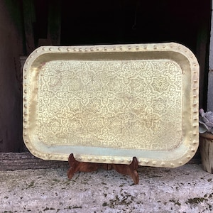 May include: A large, rectangular brass tray with a decorative, embossed pattern of stars and flowers. The tray has a raised rim and is supported by a wooden stand.