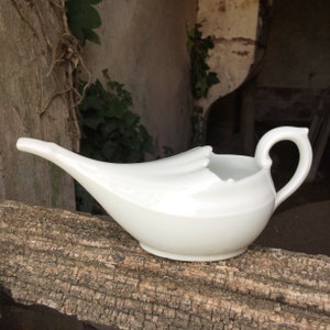 May include: White porcelain emesis basin with a spout and a handle. The basin is shaped like a curved horn.