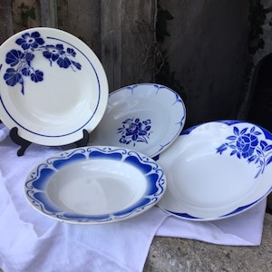 Può includere: Quattro ciotole per zuppa in ceramica bianca con motivi floreali blu. Le ciotole hanno uno sfondo bianco con motivi floreali blu e un bordo blu.