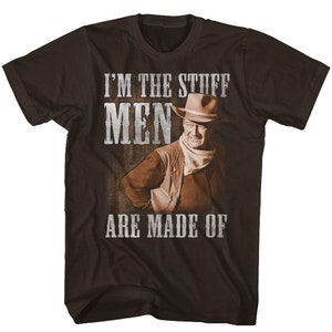 May include: A brown t-shirt with a vintage-style graphic of a cowboy wearing a hat and a bandana. The text on the shirt reads "I'm the stuff men are made of."