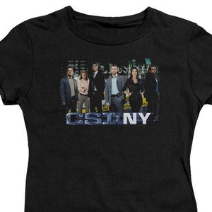 May include: Black t-shirt with a graphic of the cast of the TV show CSI: NY. The graphic features the cast members standing in front of a city backdrop. The text "CSI: NY" is printed below the graphic.