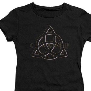 Op de afbeelding: Zwart T-shirt met een gouden en roze omtrek van een driepuntige ster met het woord "CHARMED" erin.