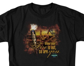 May include: A black short-sleeve t-shirt featuring a graphic of a lit torch and a skull. The text reads, "When your fire is out, so are you." and includes the Survivor logo. The design uses warm orange, yellow, and brown tones against the black fabric.
