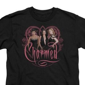 May include: Black t-shirt with a pink graphic of three women in dresses and the word "Charmed" in a stylized font.