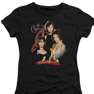 Puede incluir: Camiseta negra con un gr&aacute;fico de los tres personajes principales del programa de televisi&oacute;n "Charmed" con el t&iacute;tulo del programa en letras rosas. Los personajes est&aacute;n de pie frente a un libro en llamas.