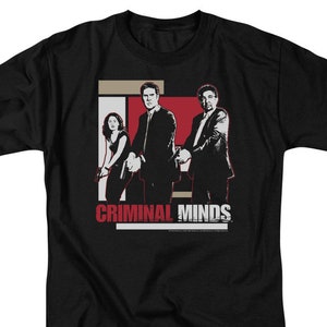 May include: Black t-shirt featuring a graphic from the television show "Criminal Minds." The design includes three figures in suits and the show's title in red and white text. The shirt is a short-sleeved crew neck.