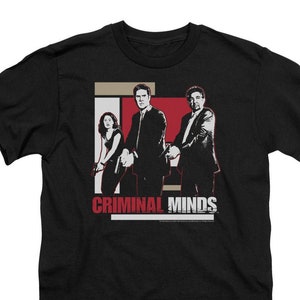 May include: Black t-shirt with a graphic of three characters from the TV show "Criminal Minds". The characters are standing in front of a red and white background. The text "Criminal Minds" is printed in white letters below the graphic.