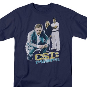 May include: Navy blue t-shirt featuring a graphic of the CSI: Miami cast. The image includes three people and the show's logo in yellow and blue. The shirt is a crew neck style.