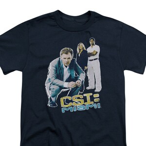 May include: A navy blue t-shirt with a graphic of three characters from the TV show CSI: Miami. The characters are standing in front of the text "CSI: Miami".