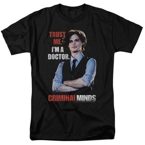 May include: Black t-shirt with a white graphic of a man in a vest and tie. The text "Trust me, I'm a doctor." is above the image and "Criminal Minds" is below the image.